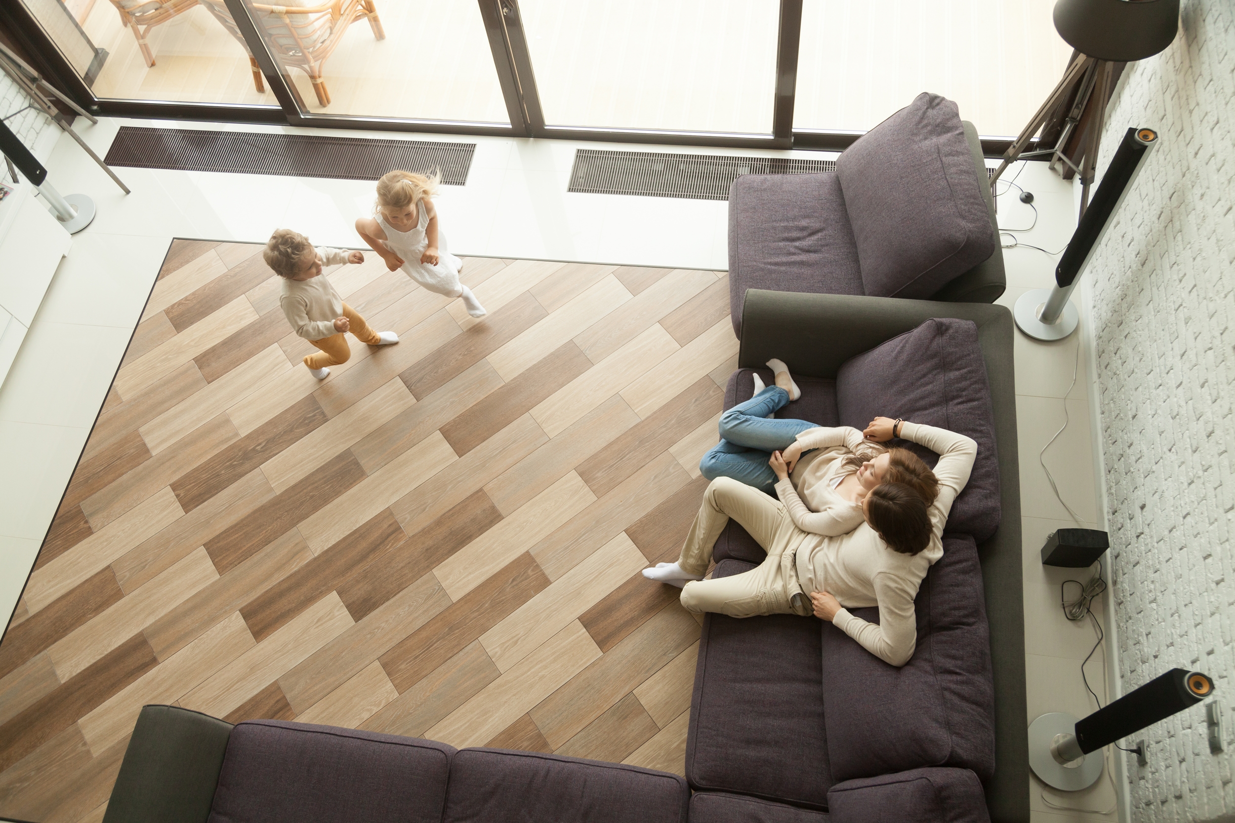 A neat and clean living room with wood patterned flooring material, in a home with a happy couple on a sofa and two young children playing and running around